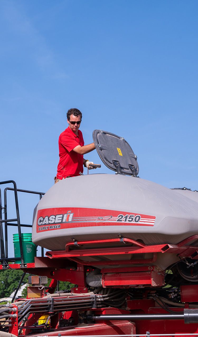 Man in a red t-shirt looks into a planter machine.